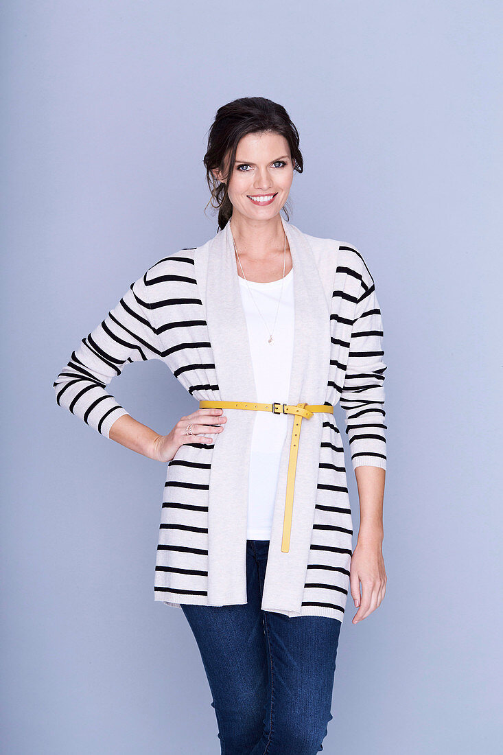 A dark-haired woman wearing a white shite, a striped cardigan and jeans