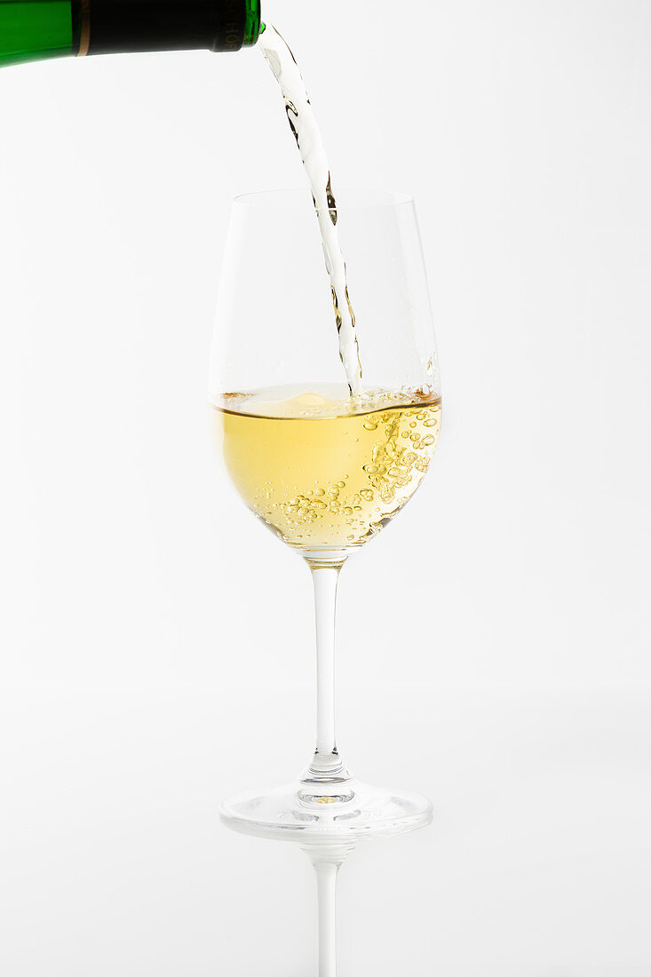 Weißwein wird aus Flasche in Glas eingeschenkt