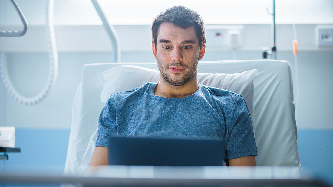 Ill patient using a laptop while lying in bed