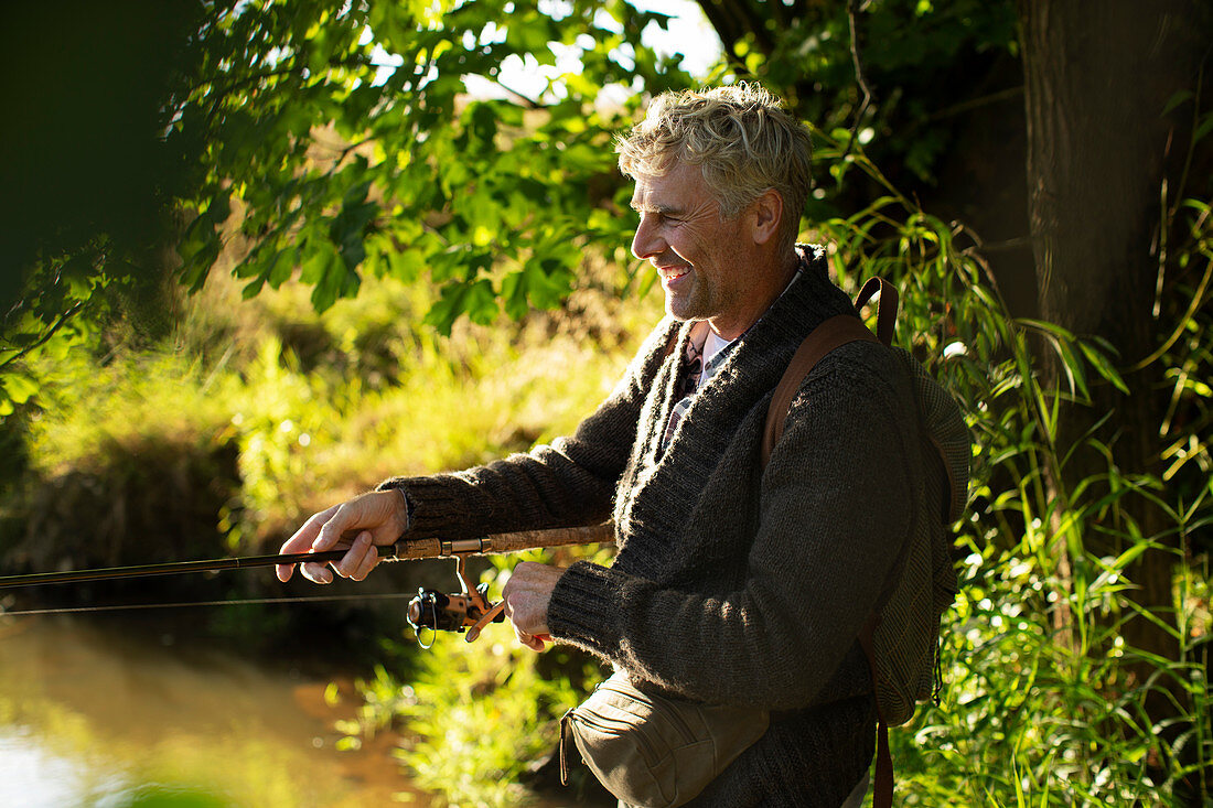 Happy man fly fishing at sunny riverbank