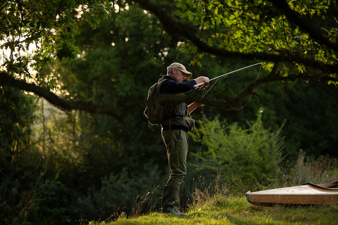 Man flying fishing under tree at riverbank