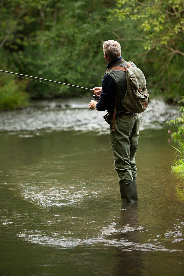 Man with backpack fly fishing at river