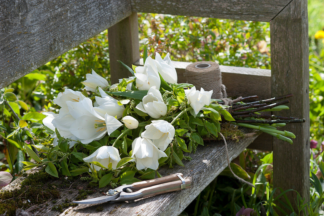 Spring bouquet of white tulips and bird cherry lying on a garden bench
