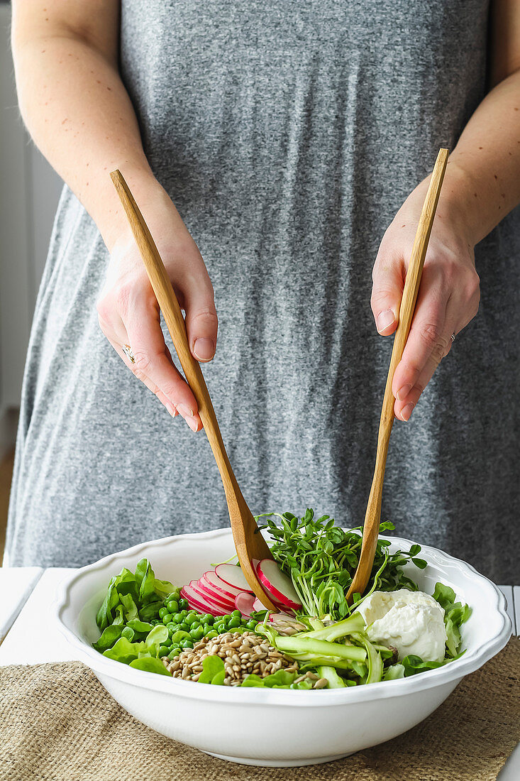 Female hands using wooden salad spoons to toss fresh spring salad