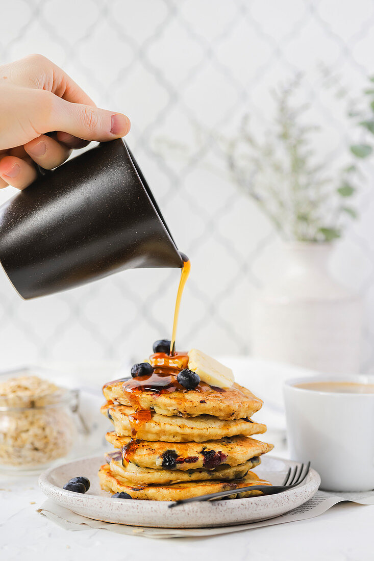 Hand pouring maple syrup on a stack of blueberry pancake