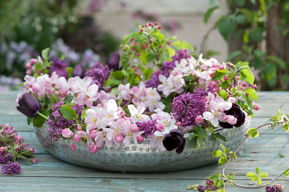 Wreath of crab apple branches, lilacs, and black tulips in a shallow silver bowl