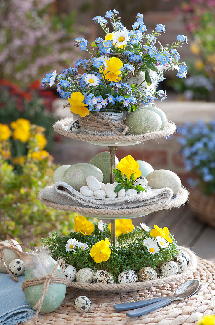 Easter table decoration: three-tier stand with small bouquets of forget-me-nots, horned violets and daisies, cress, and Easter eggs