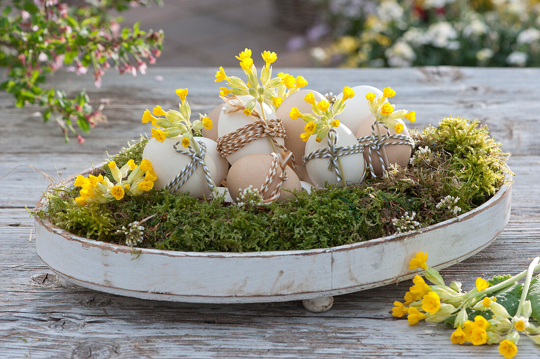 Easter eggs in a bed of moss on a wooden tray, decorated with string and primroses