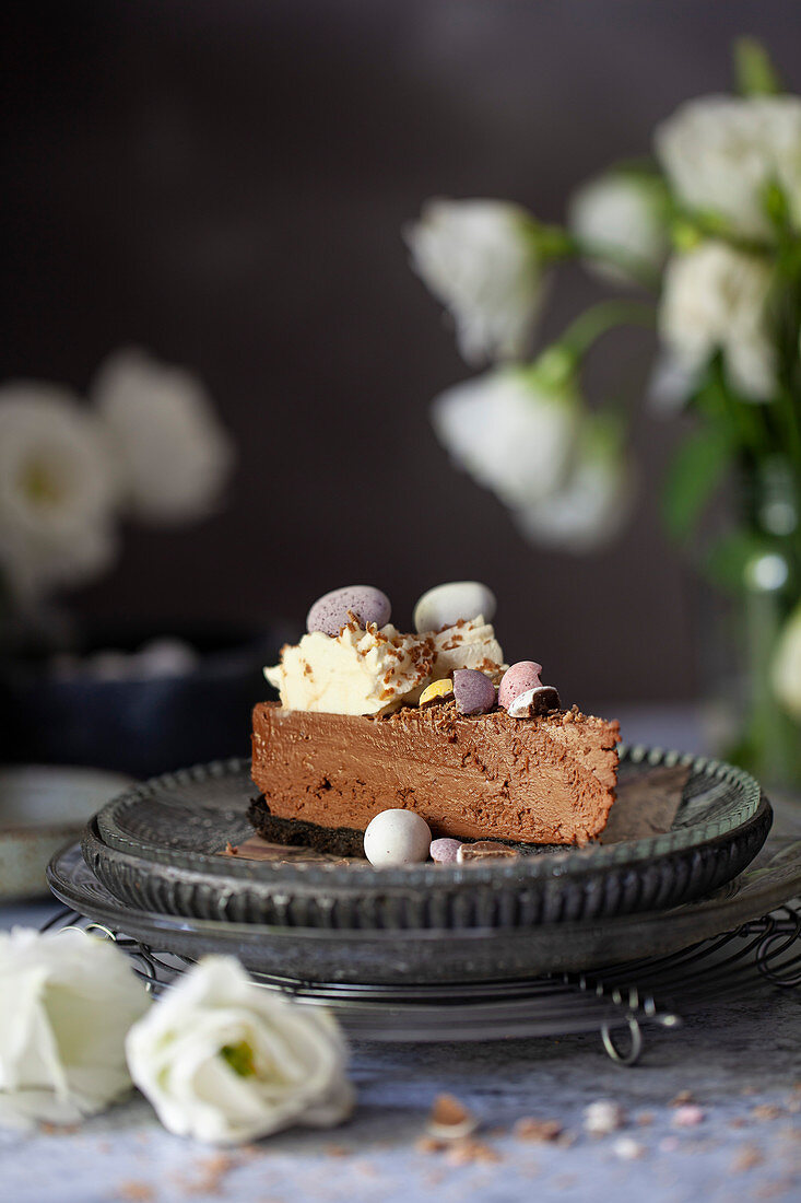 A slice of no-bake chocolate cheesecake decorated with whipped cream, chocolate flakes and candy Easter eggs
