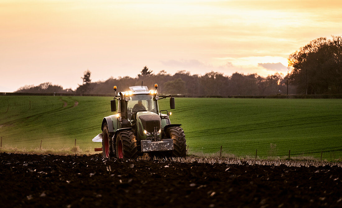 Ploughing a field at sunset with a tractor and plough, ready for crops on a farm