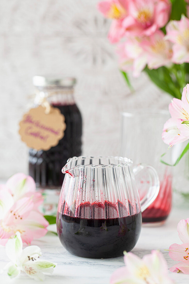 Blackcurrant cordial in a jug with some poured into a glass in the background ready for diluting with water