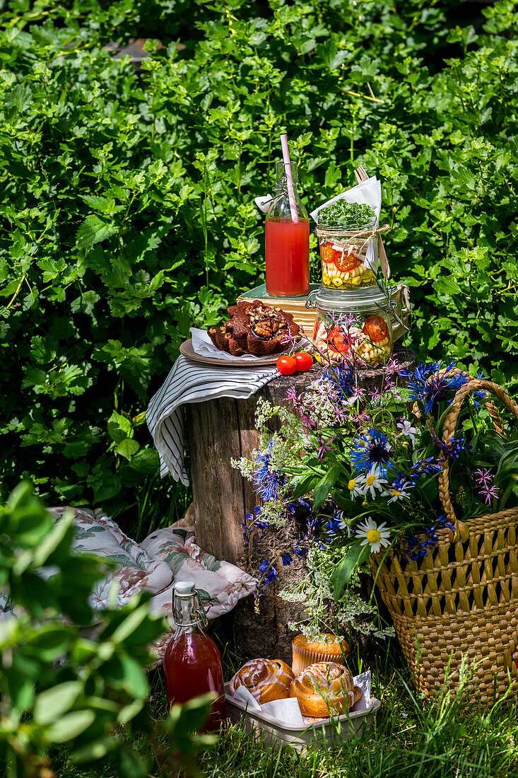 Picknick-Set auf Baumstumpf mit Salat im Glas, Limonade, Gebäck und Wildblumenstrauß