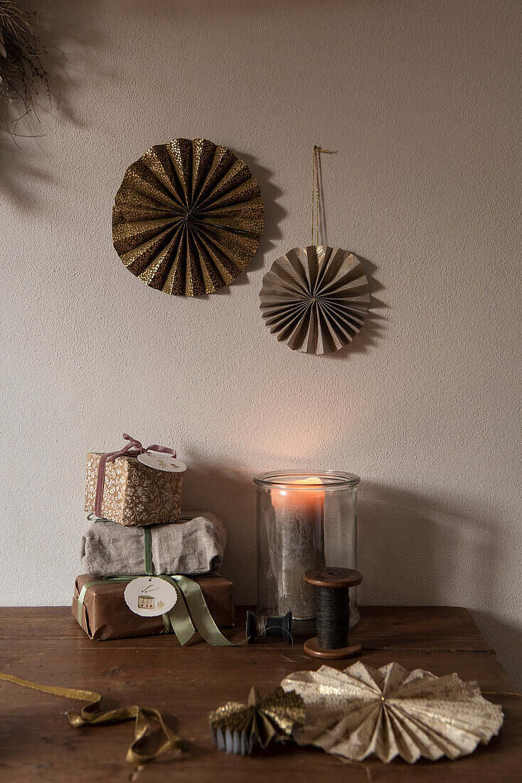 DIY-Papierrosetten über Holztisch mit verpackten Weihnachtsgeschenken und Windlicht