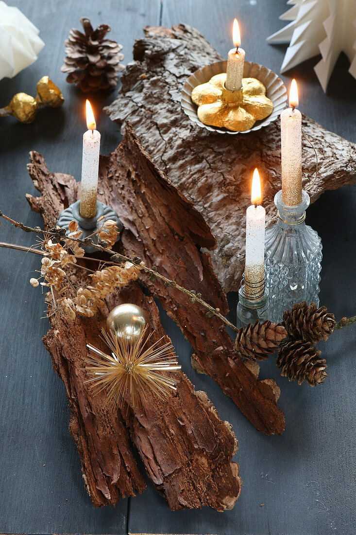 DIY Advent arrangement on tree bark decorated with burning candles on grey wood and gold Christmas tree decorations