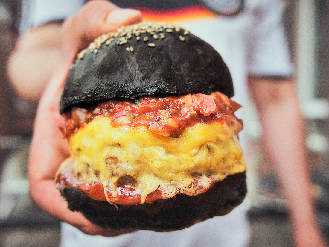 Burger smothered in melted cheese with Marinara sauce on a black seeded bun