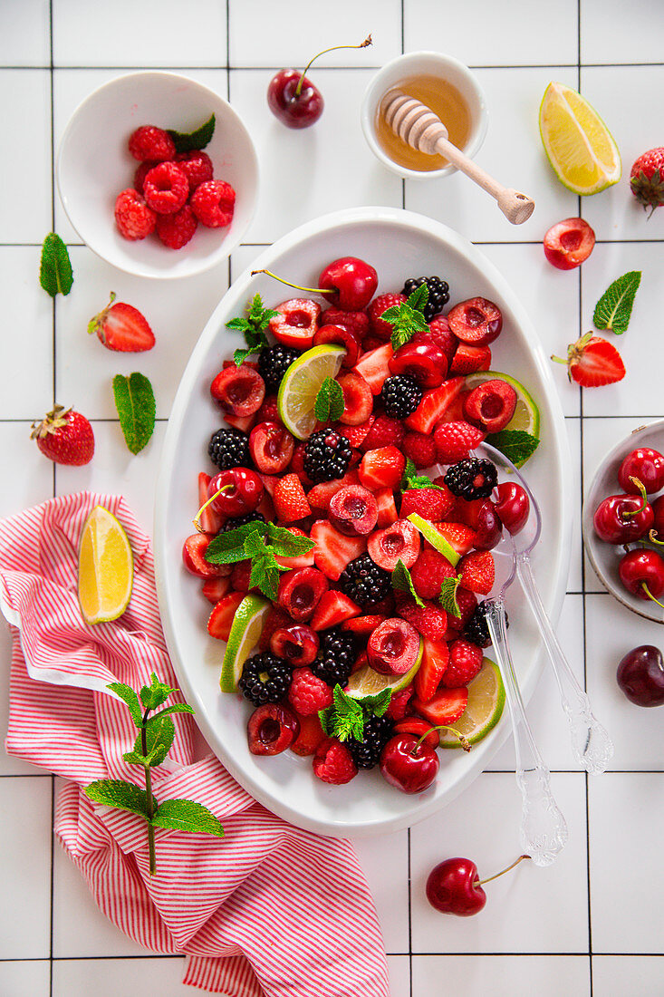 Obstsalat aus Erdbeeren, Kirschen, Brombeeren, Himbeeren, Limetten und frischer Minze