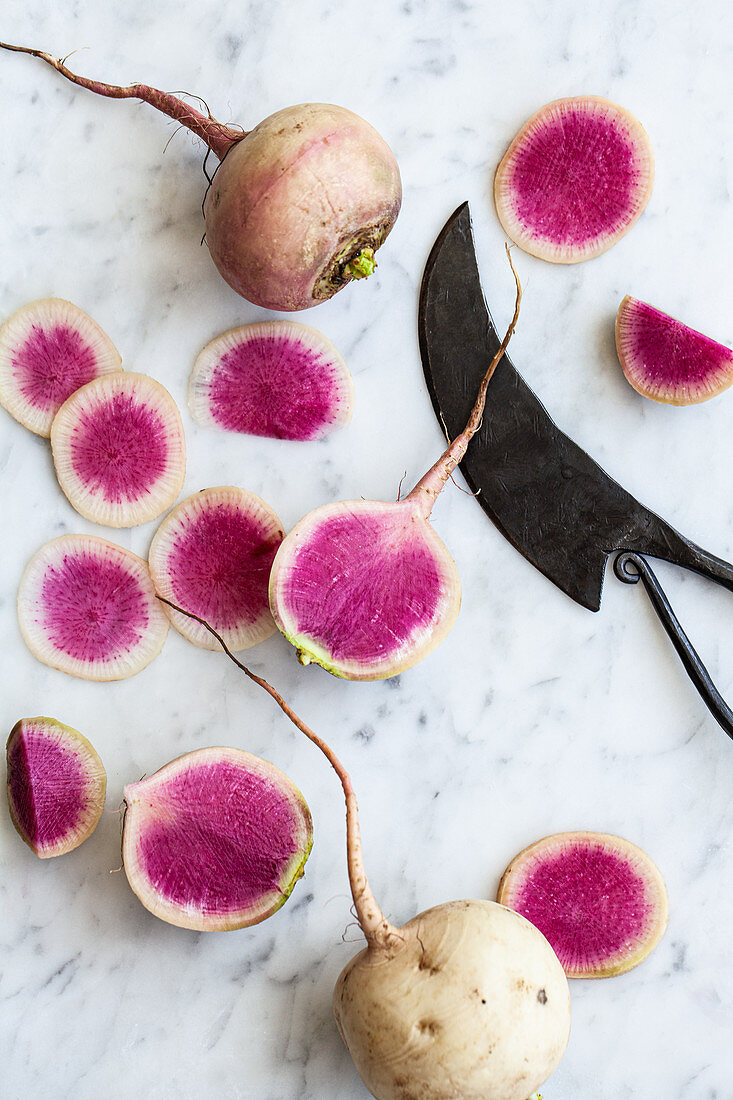 Sliced and whole watermelon radishes on a marble countertop with