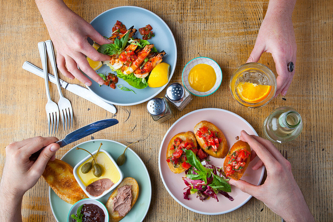 Two people, eating with with hands - Three plates of food with prawns, tomato bruschetta, and pate with bread