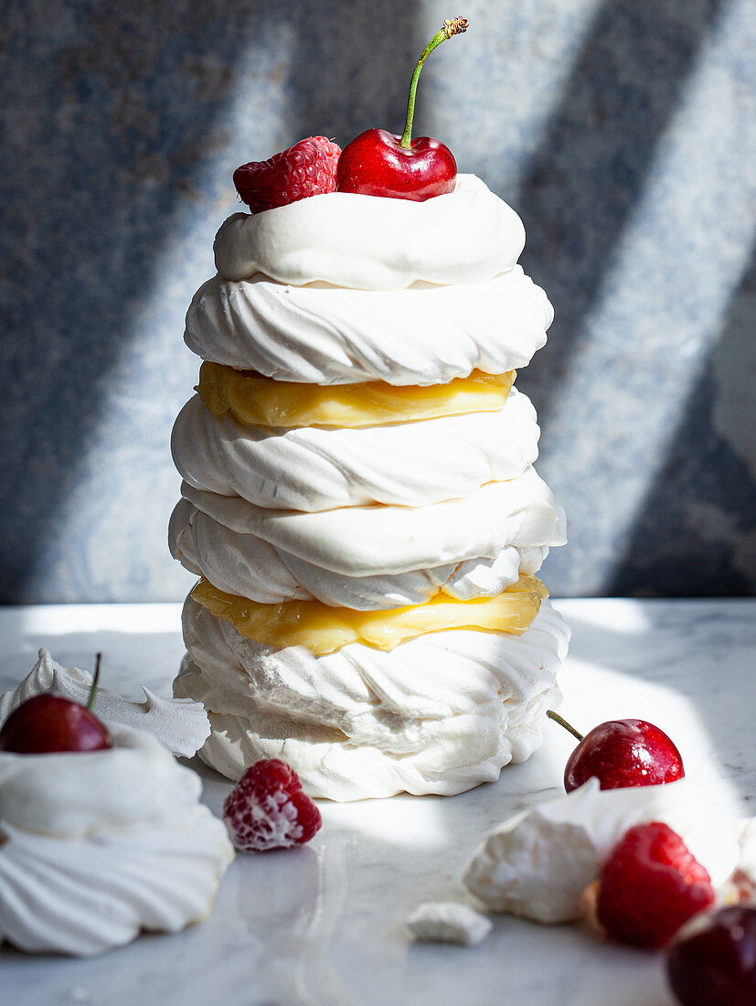 A tower of individual meringues topped with lemon curd, raspberries, whipped cream and cherries