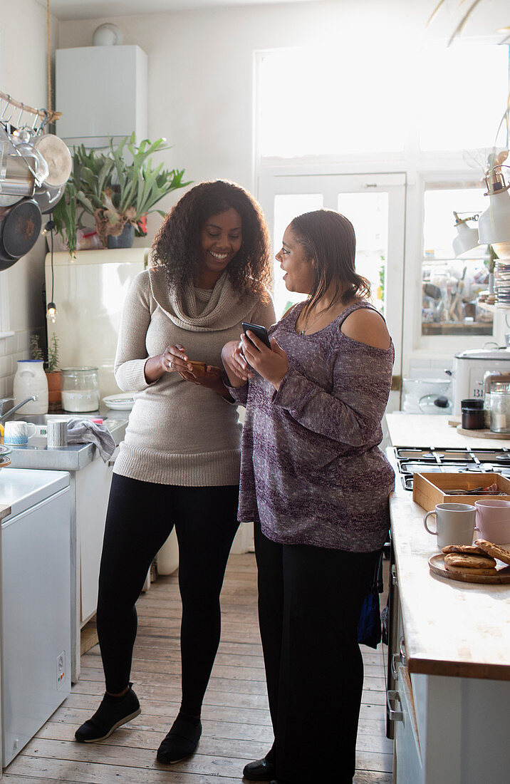 Mother and daughter using smartphones in kitchen
