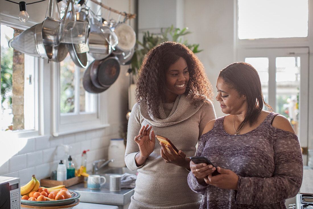 Mother and daughter using smartphones in kitchen