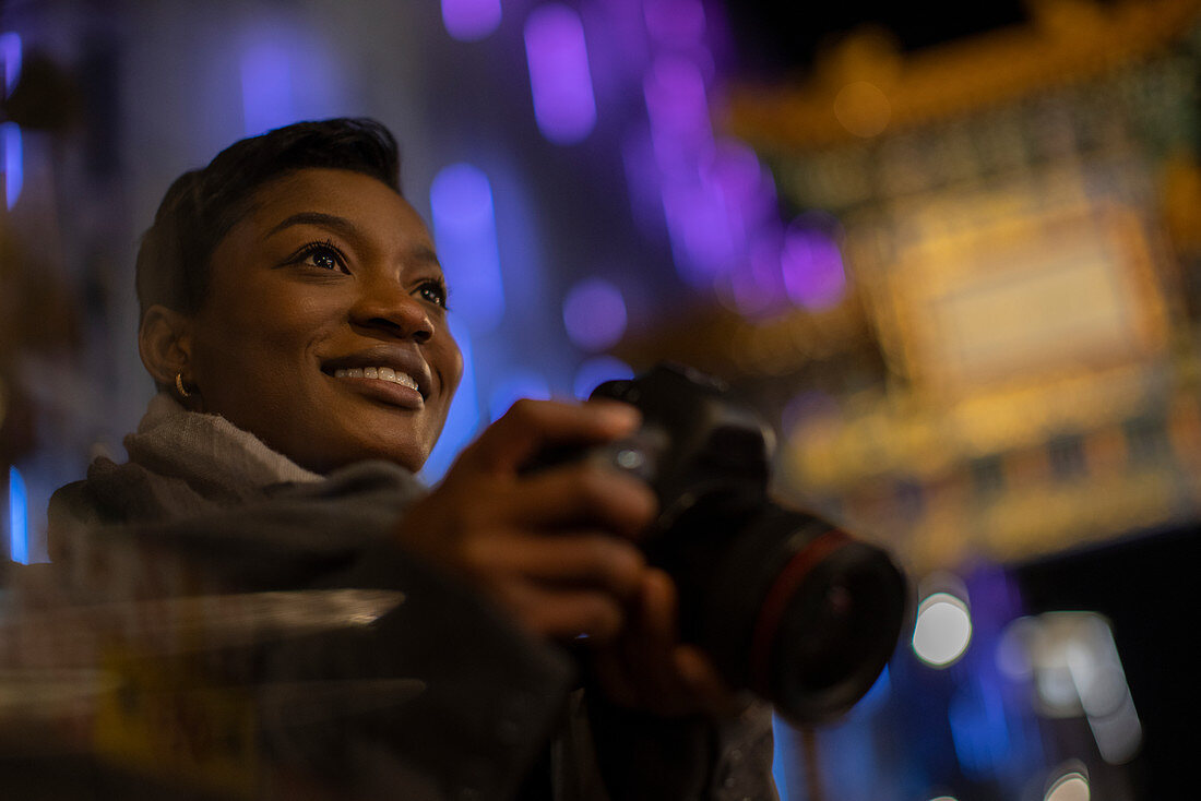 Happy young woman with camera in city at night