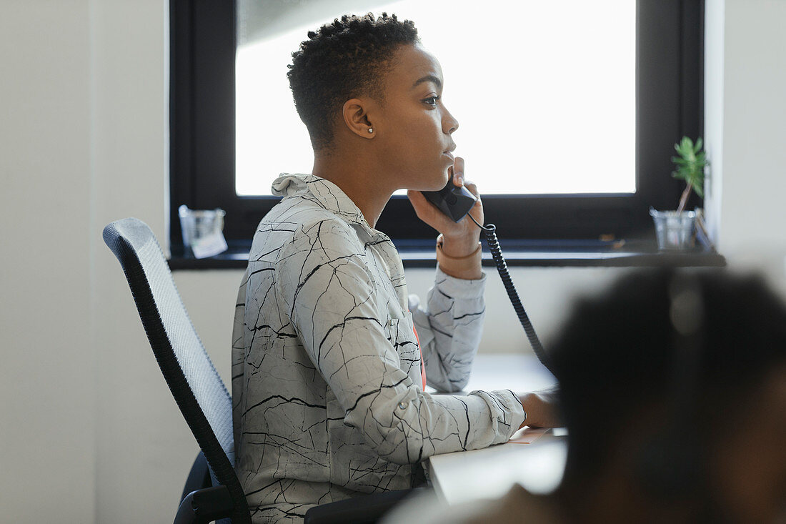 Businesswoman talking on telephone at office window