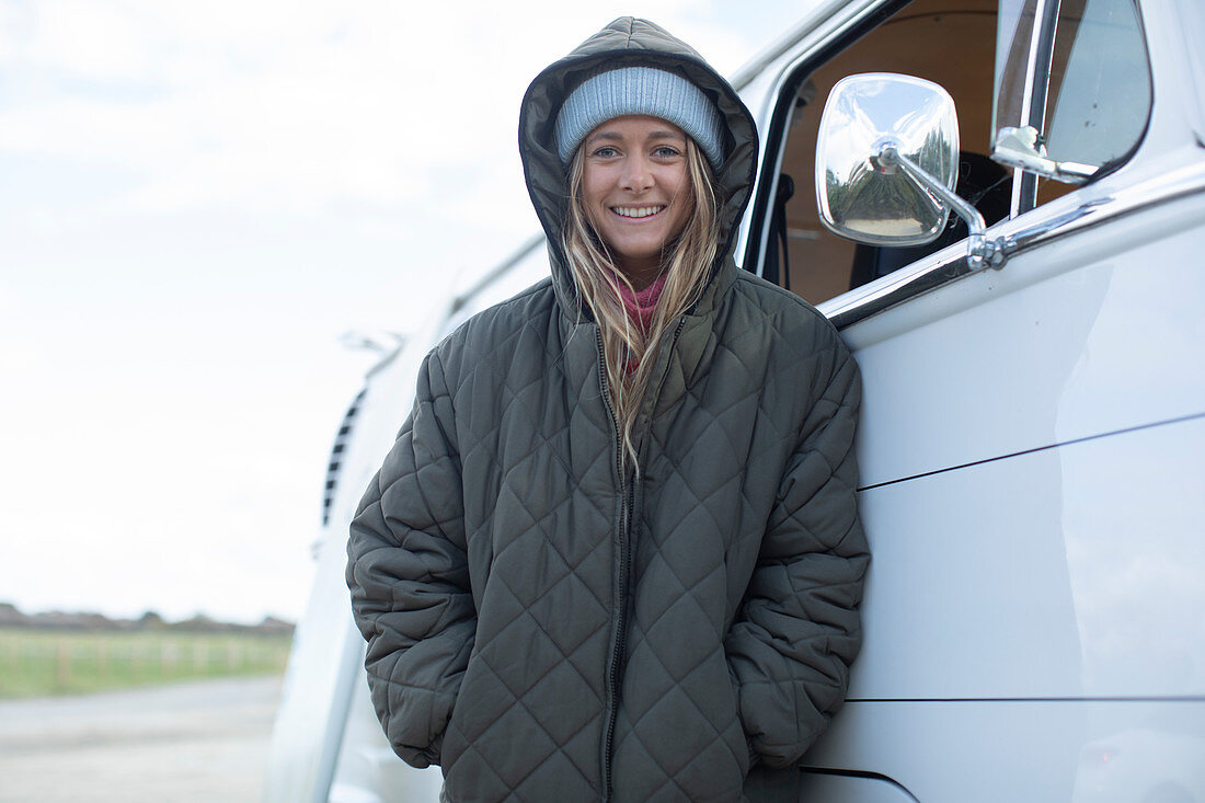 Happy young woman in hooded coat outside van