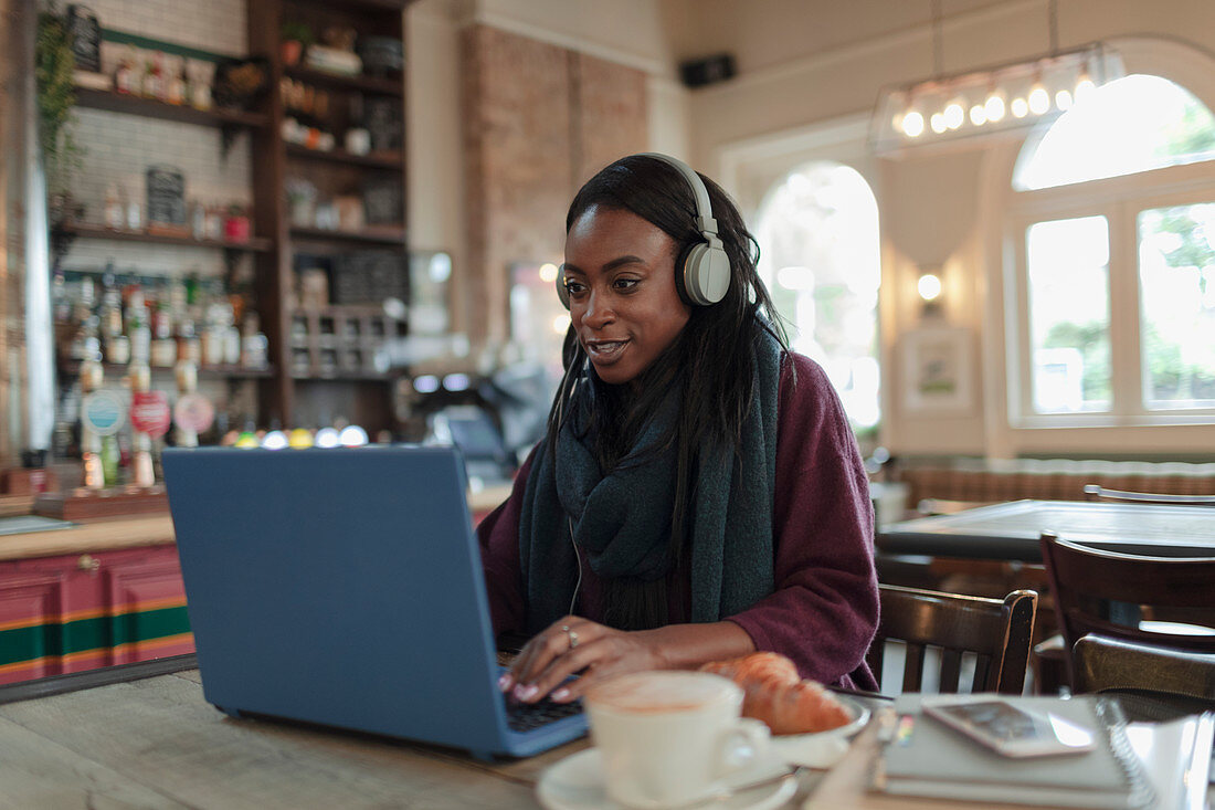 Woman with headphones working at laptop on cafe table