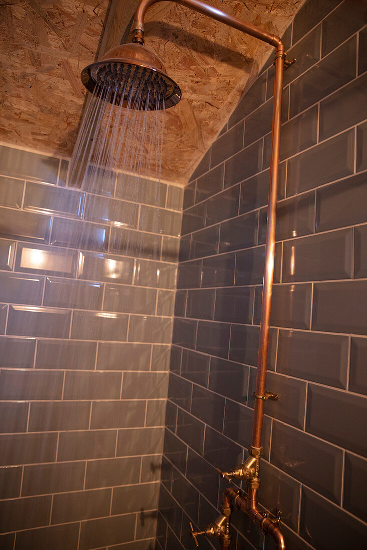 Water spraying from copper shower head in tiled shower
