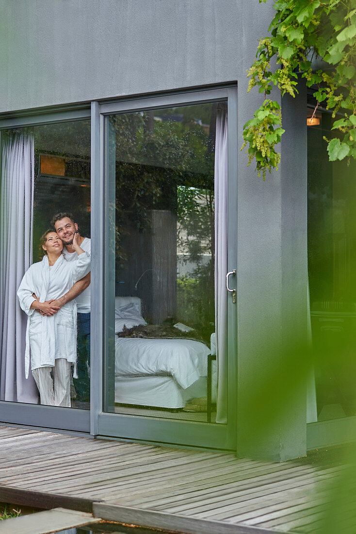 Affectionate couple standing at morning bedroom window