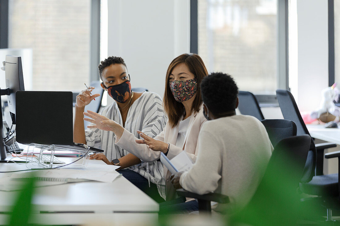 Business people in face masks talking in office meeting