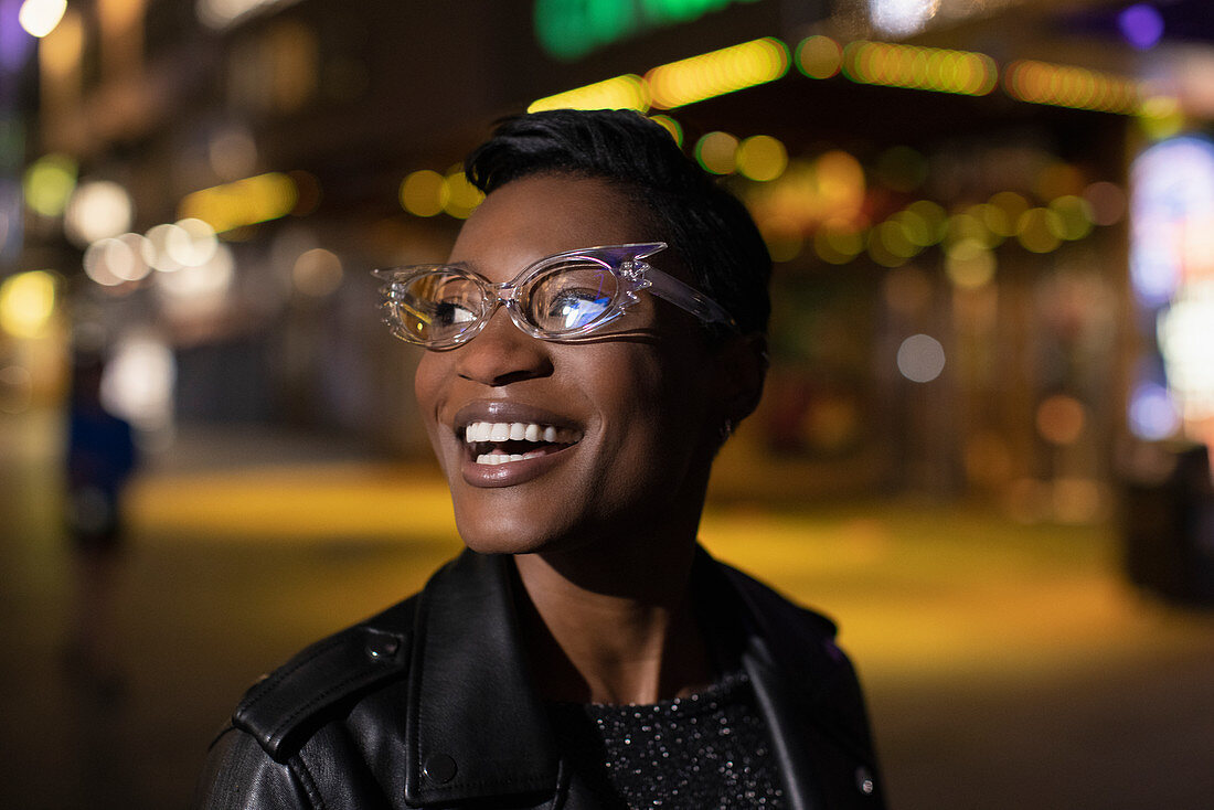 Happy young woman in funky glasses on city street at night