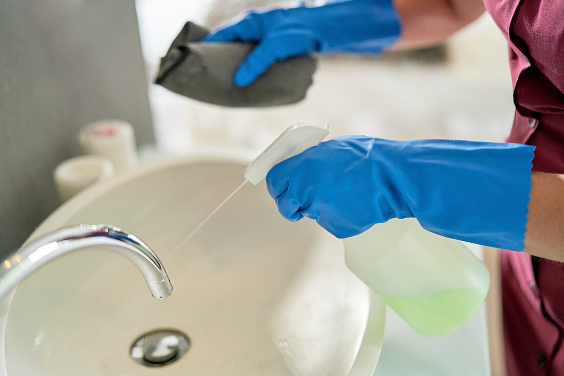 Hotel maid in gloves spray cleaning bathroom sink
