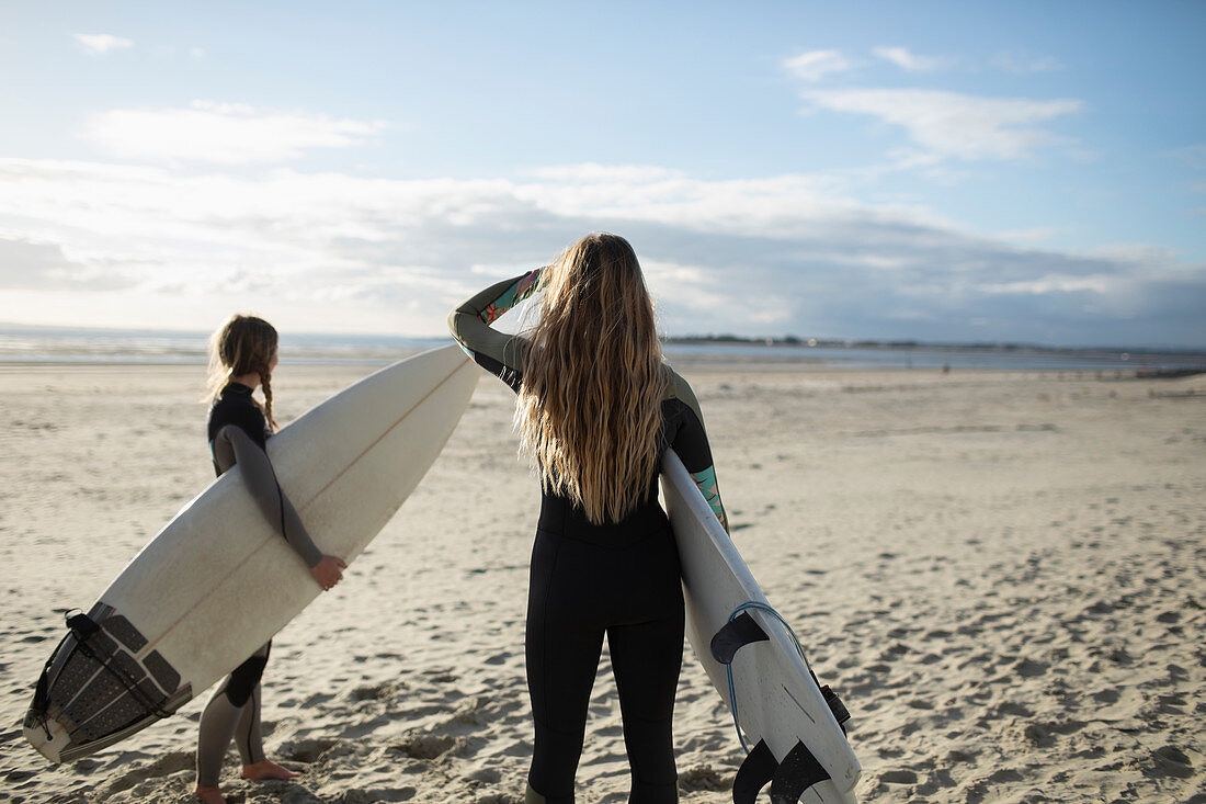Young female surfers with surfboards on sunny summer beach