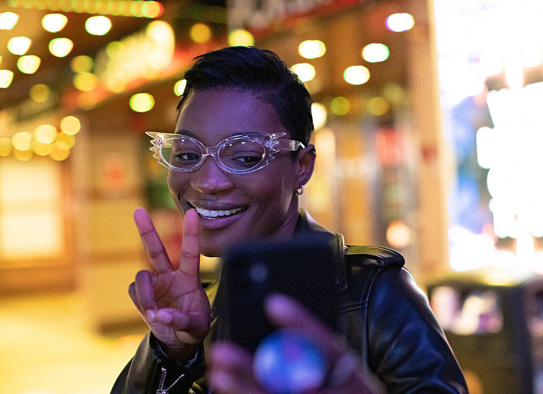 Young woman in funky eyeglasses taking selfie at night