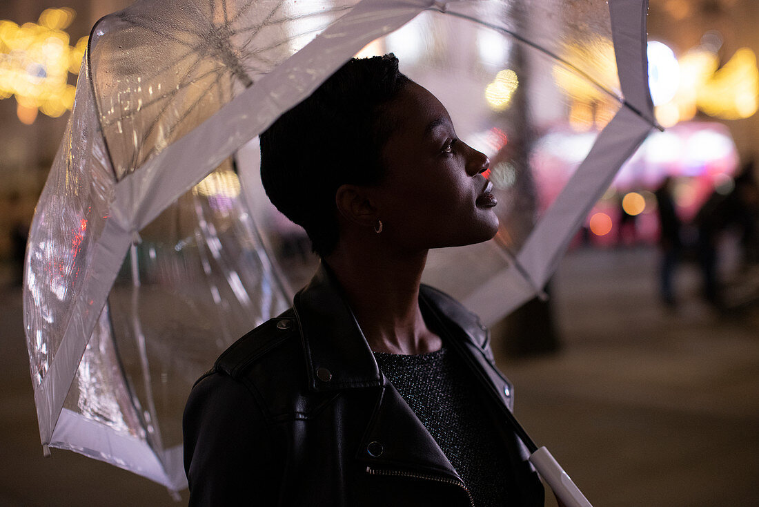 Young woman under umbrella on city sidewalk at night