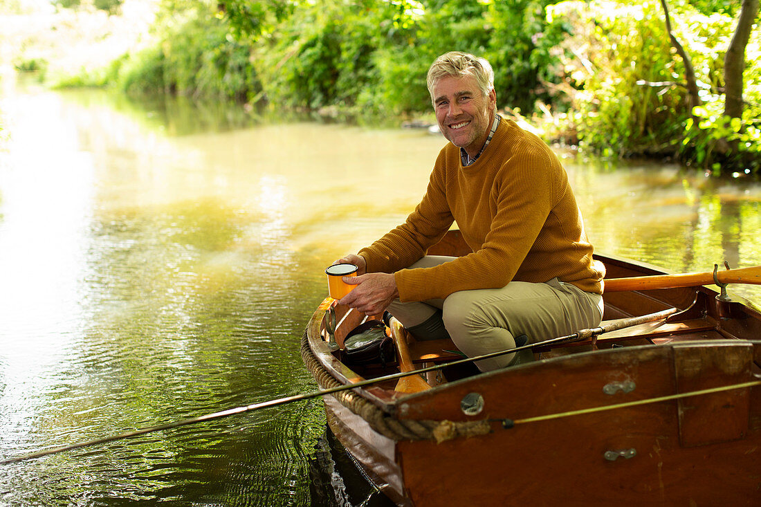 Happy man with coffee fly fishing in boat on river