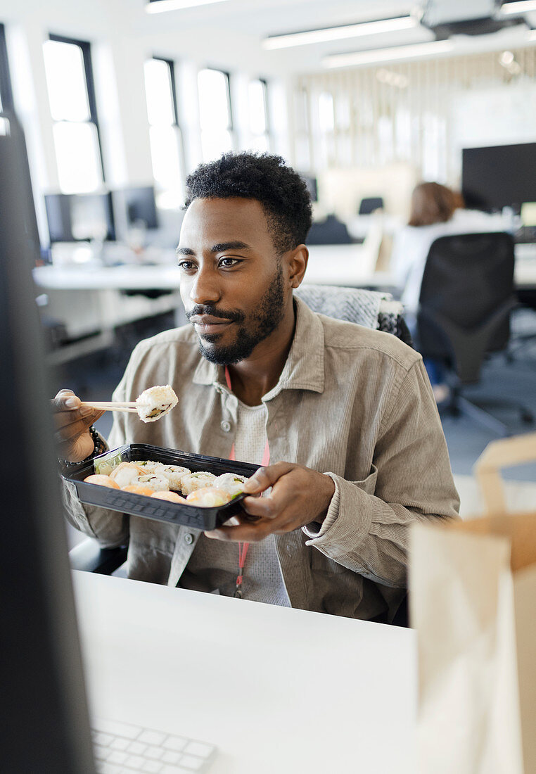 Businessman eating takeout sushi lunch at computer in office