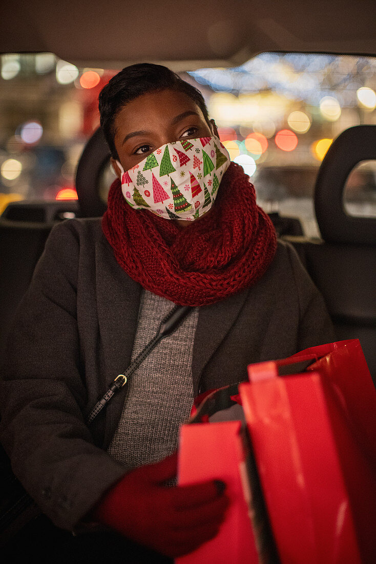 Young woman in Christmas facemask with shopping bags in taxi