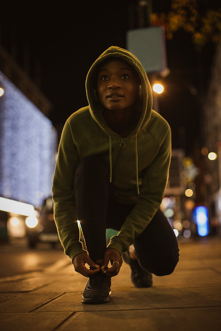 Female runner tying shoelace on urban sidewalk at night