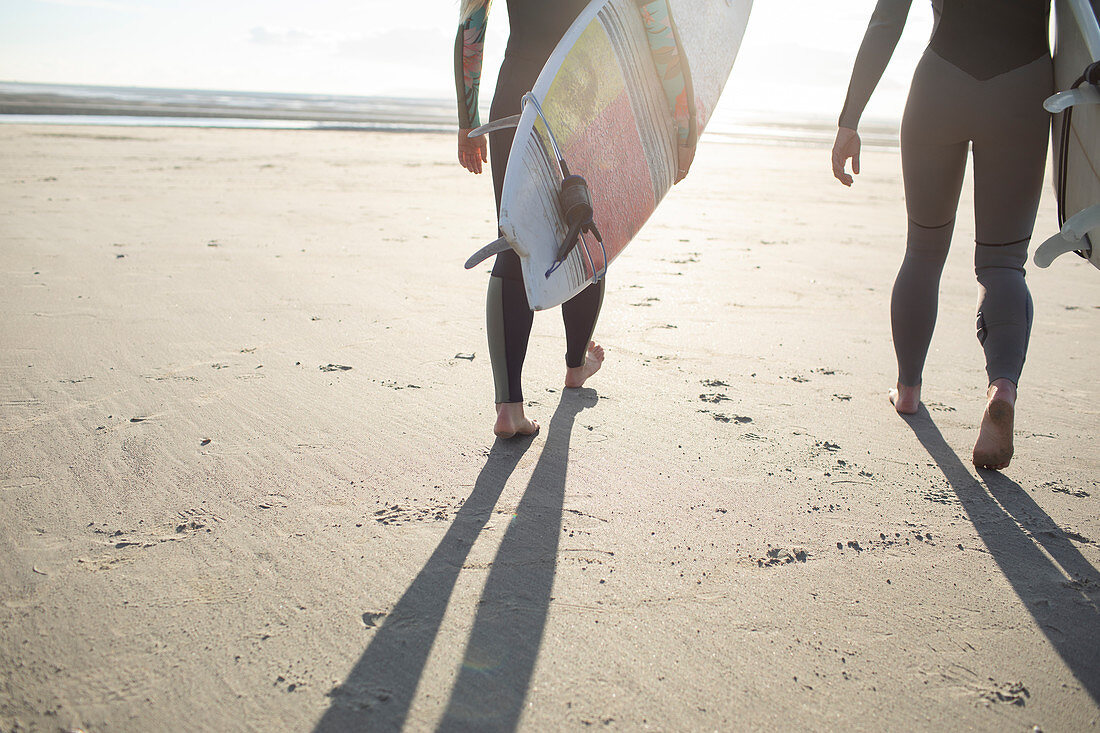 Female surfers carrying surfboards on sunny sandy beach
