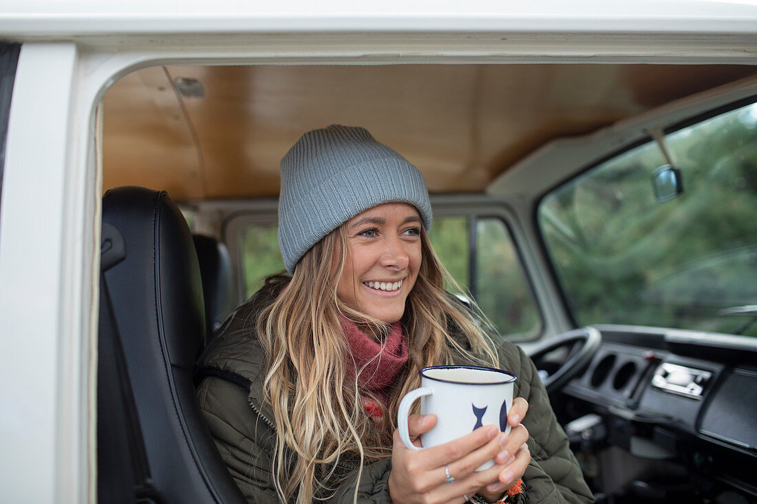 Happy young woman drinking coffee in camper van doorway