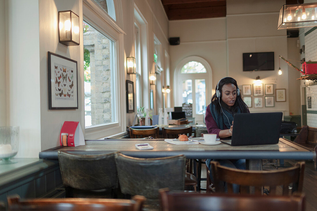 Businesswoman with headphones working at laptop in cafe
