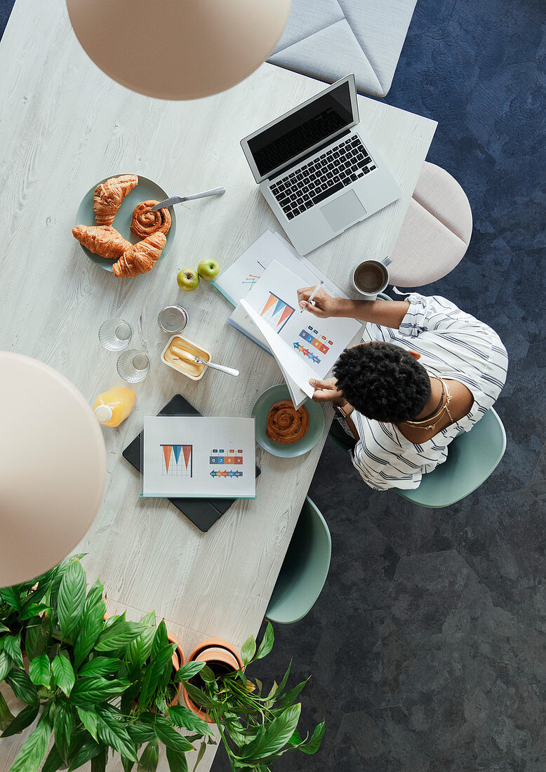 Businesswoman reviewing paperwork at breakfast in office