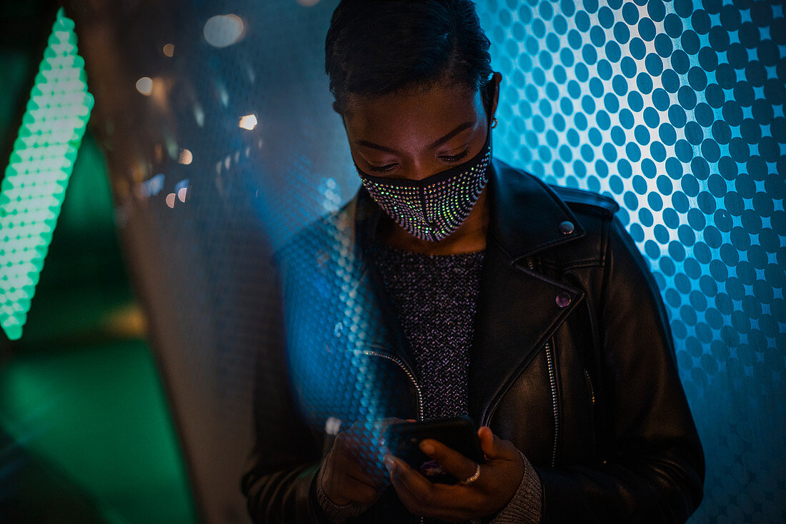 Young woman in face mask using smartphone in blue light