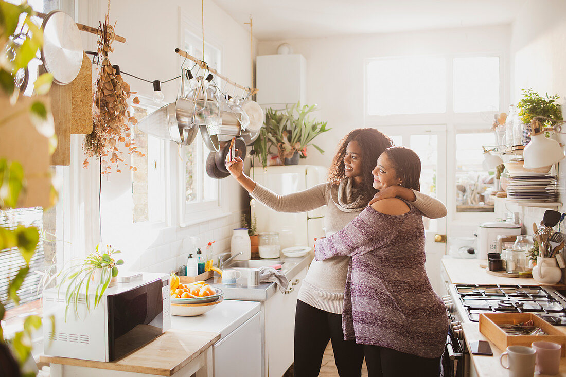 Happy mother and daughter taking selfie in sunny kitchen