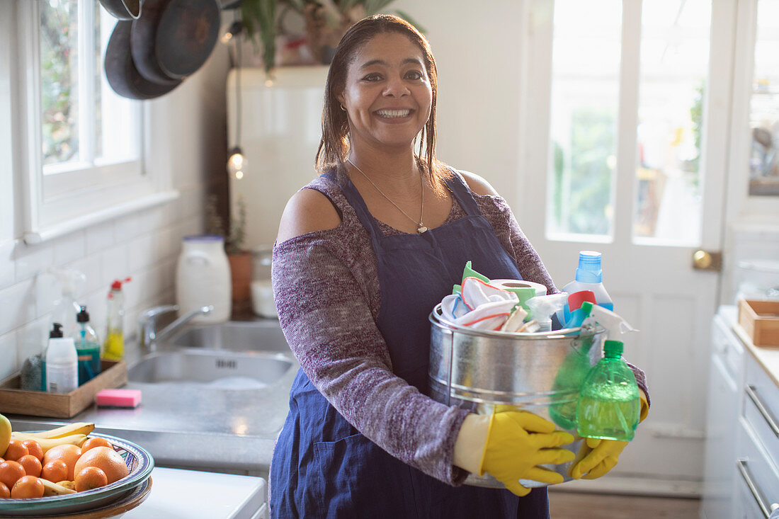 Smiling woman with cleaning supplies in kitchen