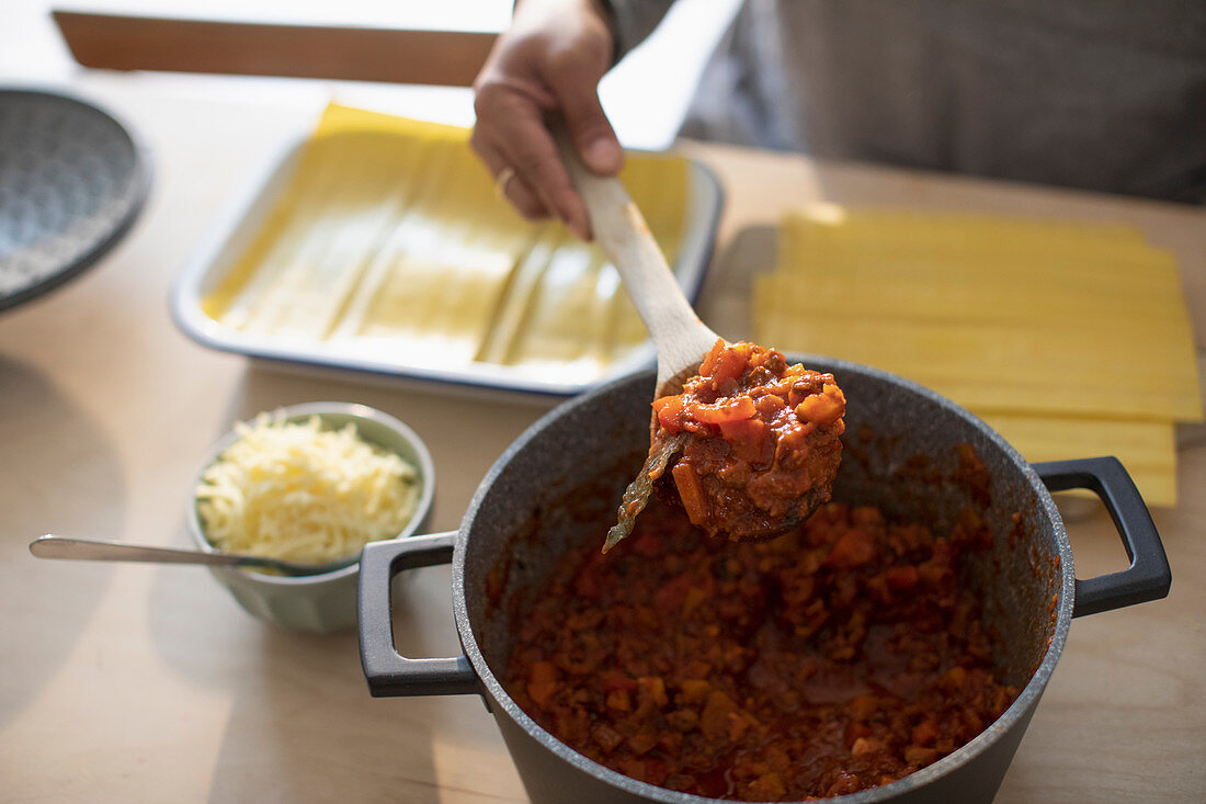 Woman with tomato sauce making fresh lasagne at home