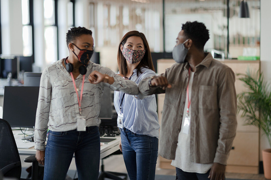 Business people in face masks elbow bumping in office